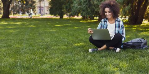 Young woman with laptop sitting on grass